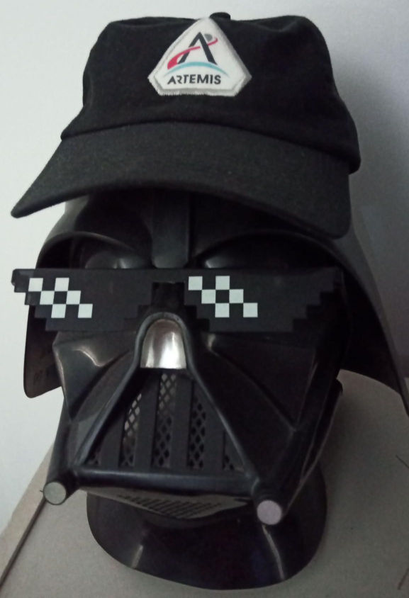 My Artemis II hat, being worn by my Darth Vader helmet, which is also wearing thug life pixelated sunglasses
